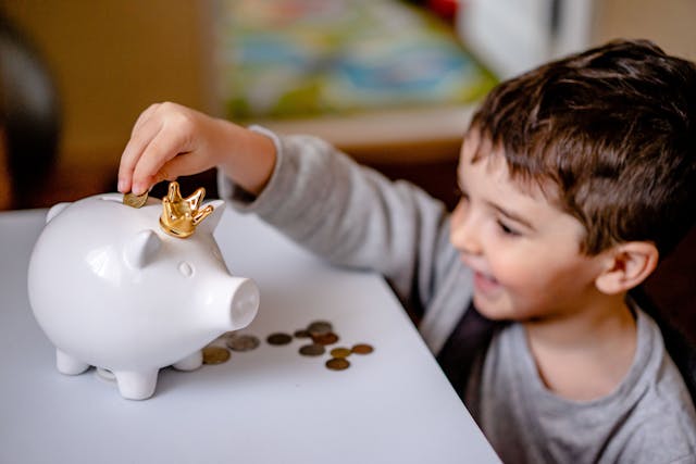 A child putting a coin into a piggy bank Description automatically generated