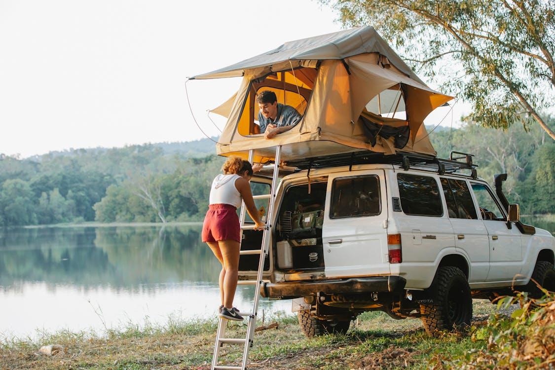 woman standing on ladder near husband recreating in tent during camping at lakeside Stock Photo