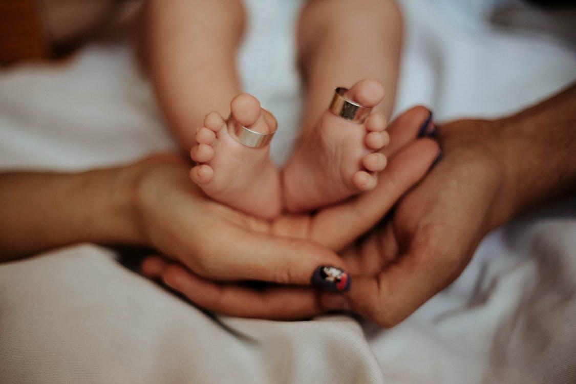 Parents holding their baby’s feet, with wedding rings gently placed on the baby’s toes.