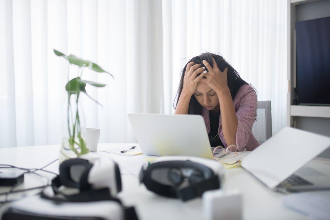 Free Frustrated woman sitting at desk with laptop, showing stress in a modern office environment. Stock Photo