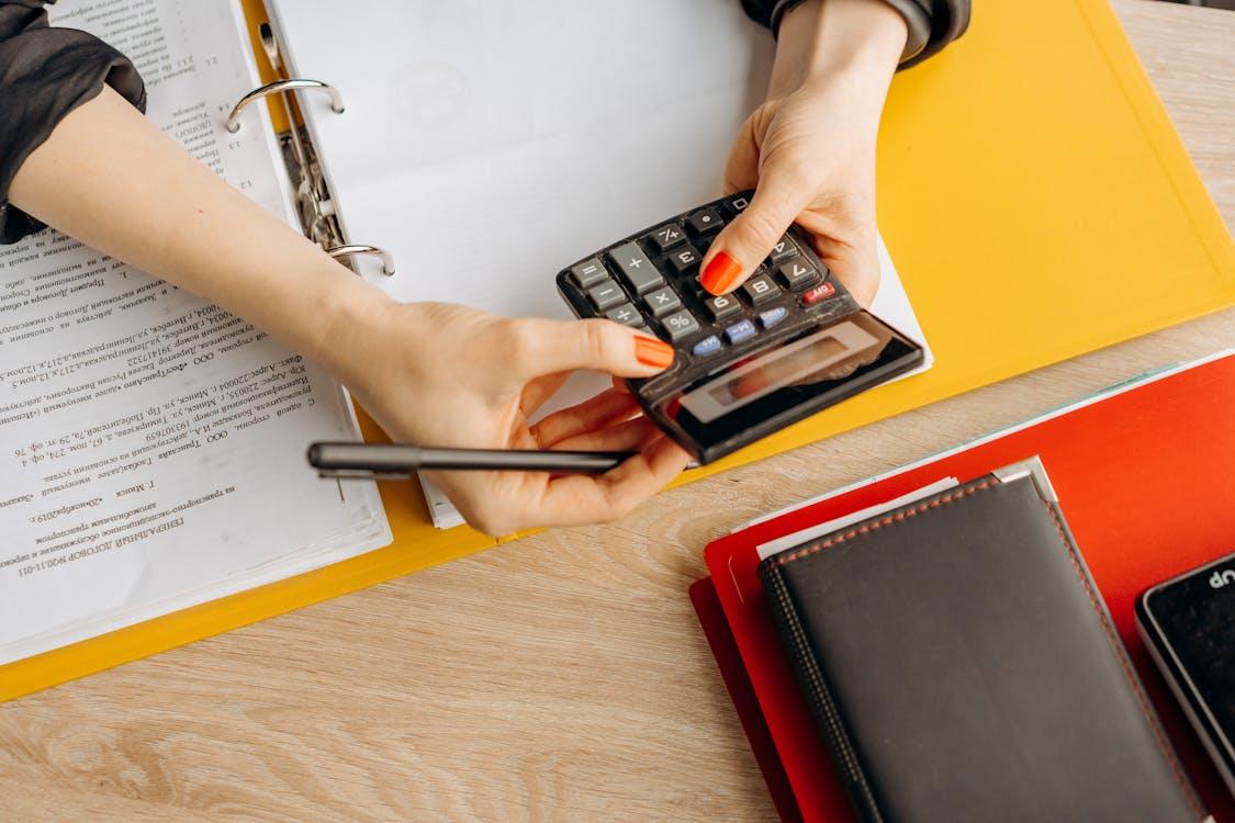 navigating perimenopause: Free Hands using a calculator at a desk with documents and folders, ideal for finance or accounting themes. Stock Photo