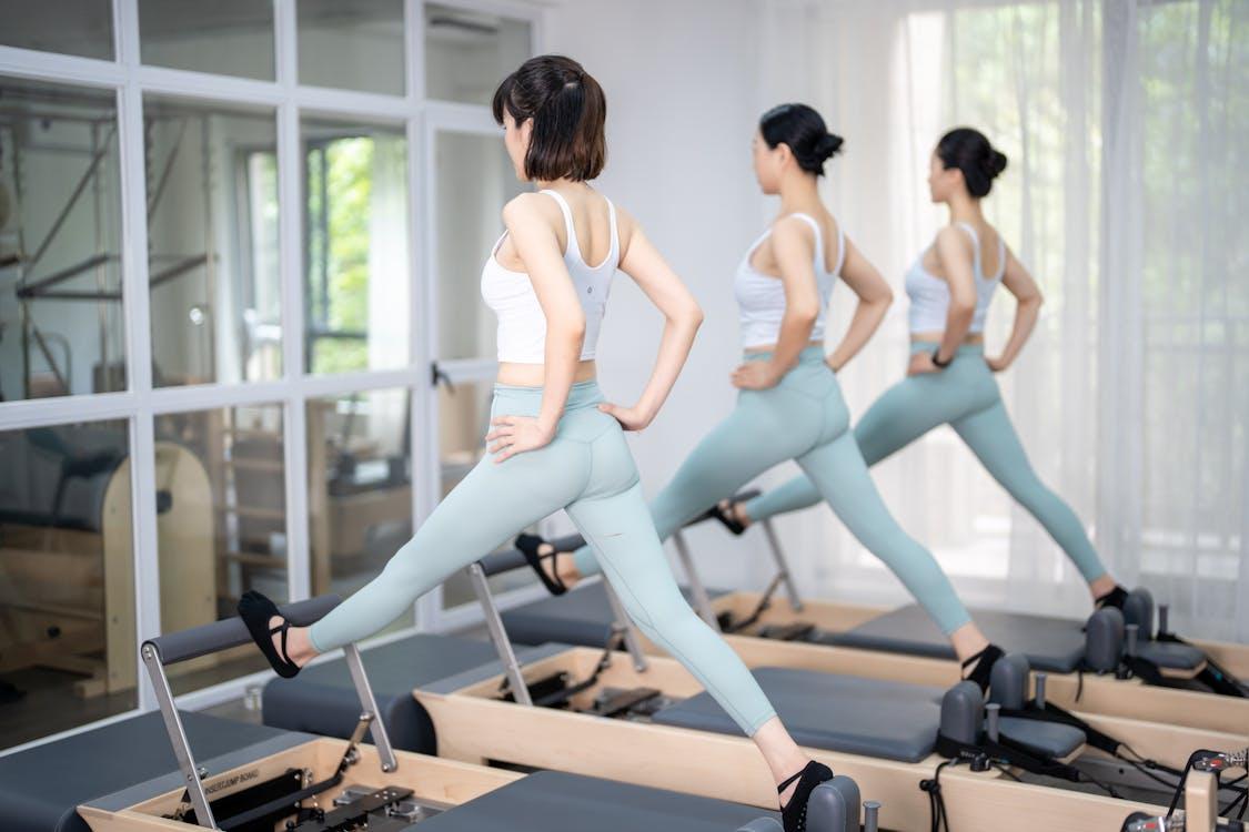 navigating perimenopause: Free Three women in athletic wear exercising on Pilates reformers indoors, promoting a healthy lifestyle. Stock Photo